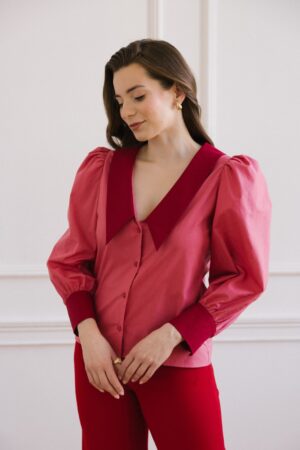 Różowa koszula z bufkami i czerwonym długim kołnierzem oraz mankietami połączona z czerwonymi spodniami.