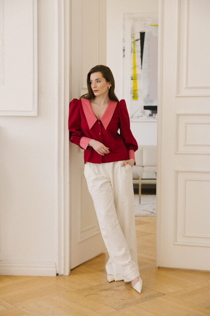 Czerwona koszula damska z bufkami i różowym kołnierzem oraz mankietami w połączeniu z szerokimi jasnymi, lnianymi spodniami