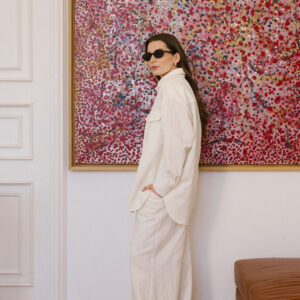 Lniana oversizowa koszula damska. Kobieta zwrócona bokiem w lnianym komplecie damskim w kolorze ecru/złamanej bieli